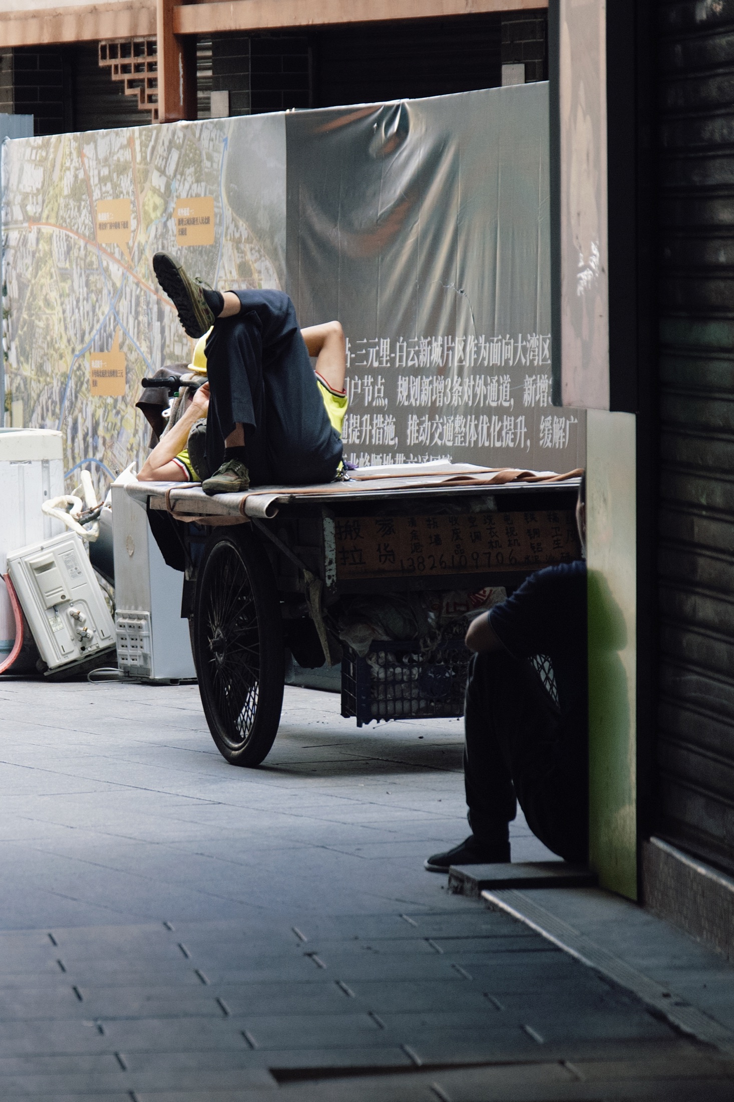 施工围挡旁，一位工人蜷坐在手推车上休息