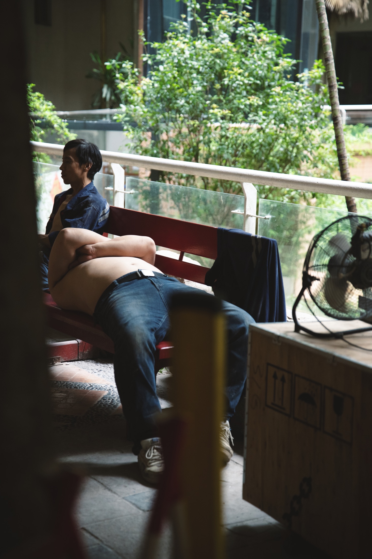 一名男子躺在长椅上休息，旁边的风扇正在转动
